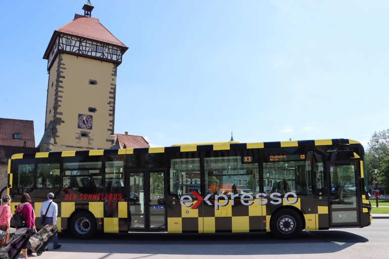 Menschen gehen mit einem Koffer auf den neuen eXpresso Bus zu